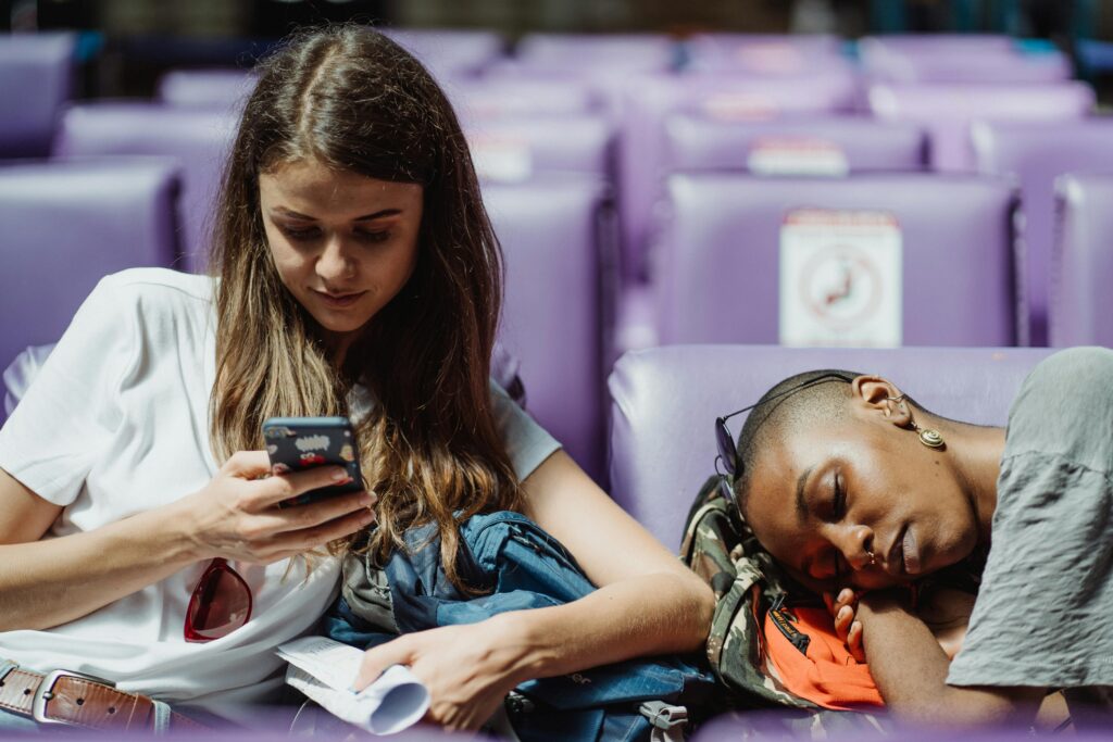 person looking at a phone while a 2nd person has fallen asleep in a seat