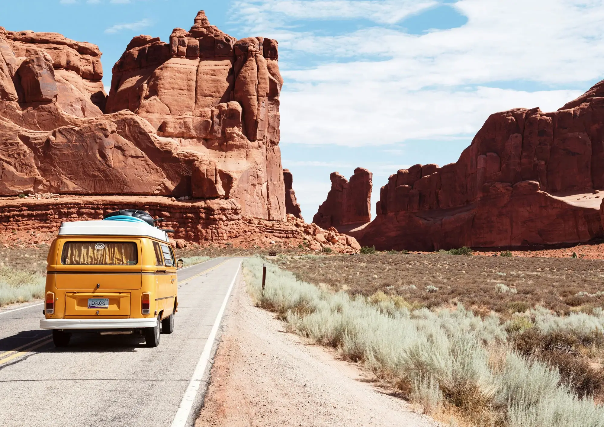 yellow camper driving through red rocks